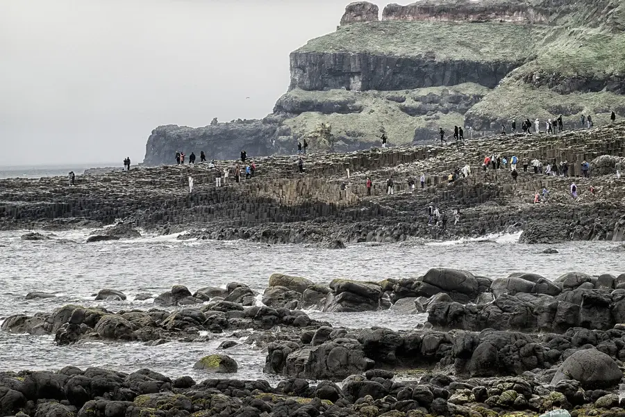 Visiteurs marchant sur les dalles de la Chauss&eacute;e des G&eacute;ants au pied de la falaise