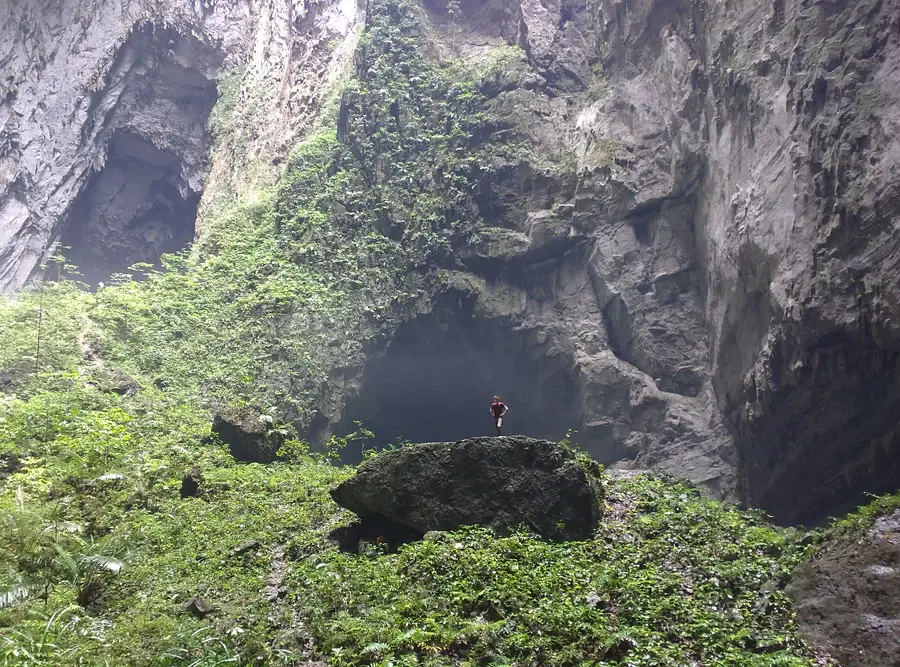 Personne debout au pied de la paroi d&rsquo;une doline, minuscule &agrave; l&rsquo;&eacute;chelle de la cavit&eacute;
