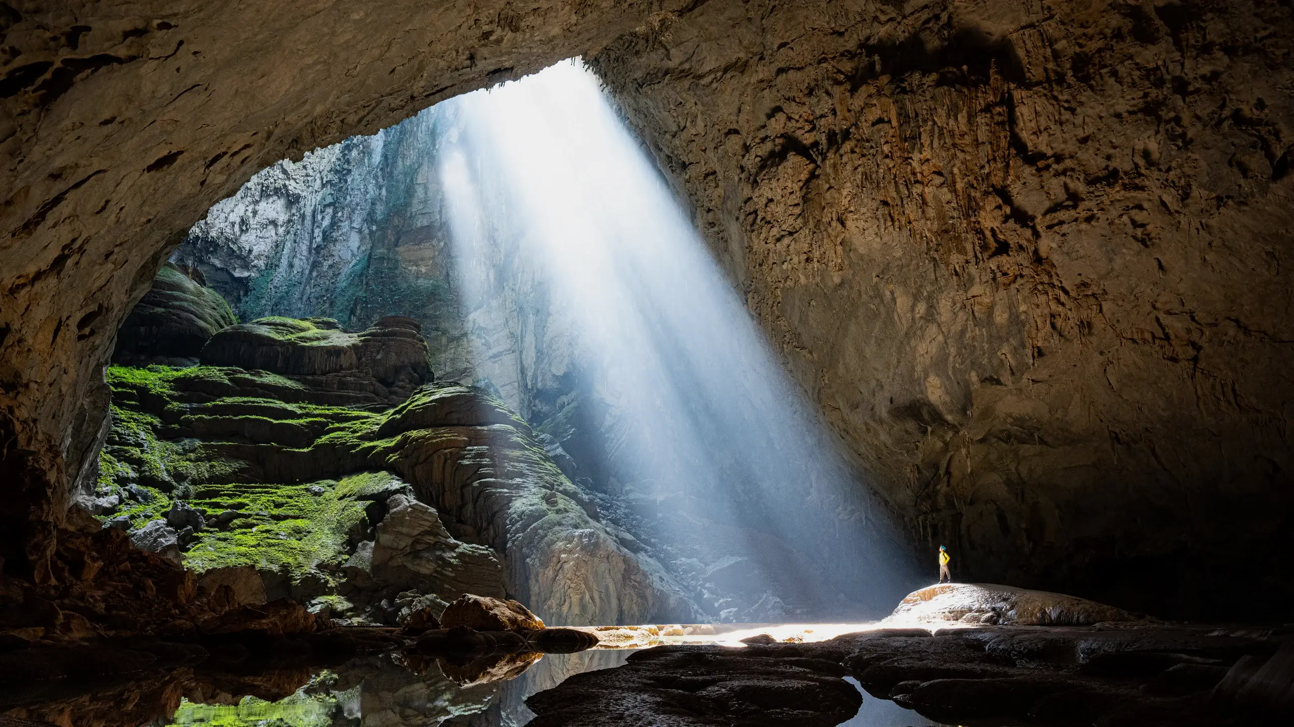 Rayon de lumi&egrave;re traversant la doline de la grotte de Sơn Đo&ograve;ng, silhouette humaine sur un rocher