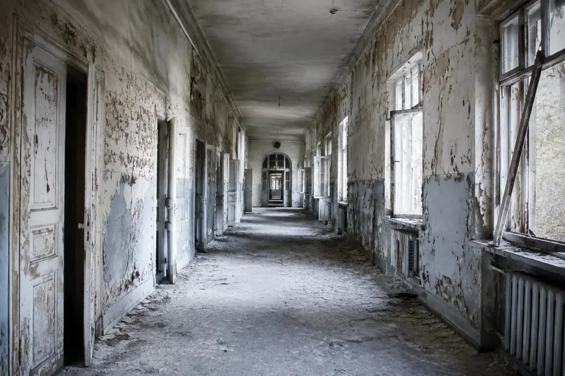 Hôpital psychiatrique abandonné : couloir intérieur vide, murs décrépis et lumière froide dans un bâtiment délaissé