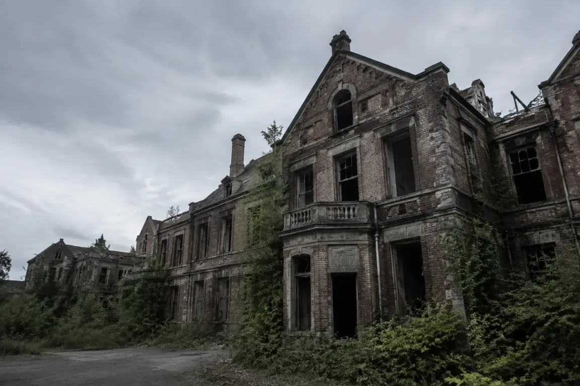 Hôpital psychiatrique abandonné : façade extérieure d’un bâtiment déserté, fenêtres brisées et végétation envahissante